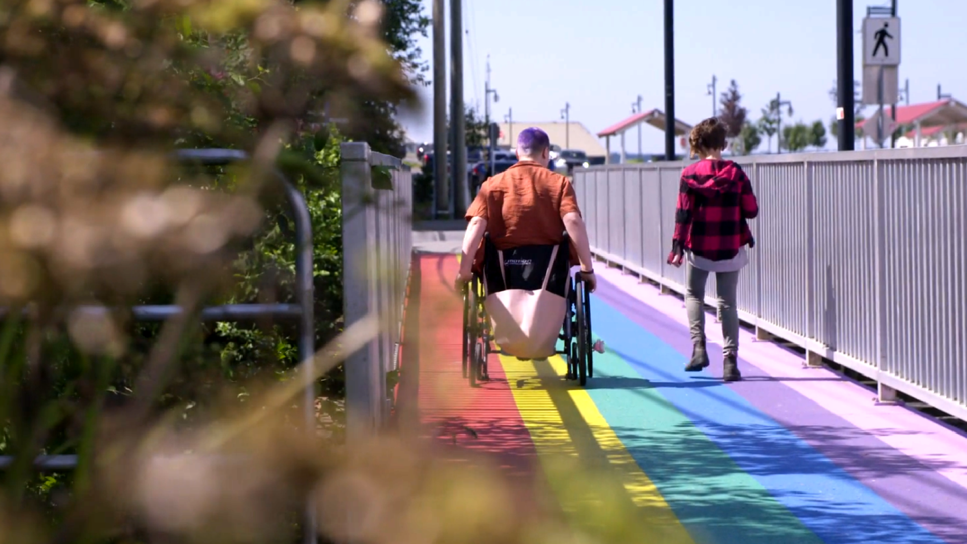 A child and a wheelchair user crossing the rainbow painted bridge in Cow Bay